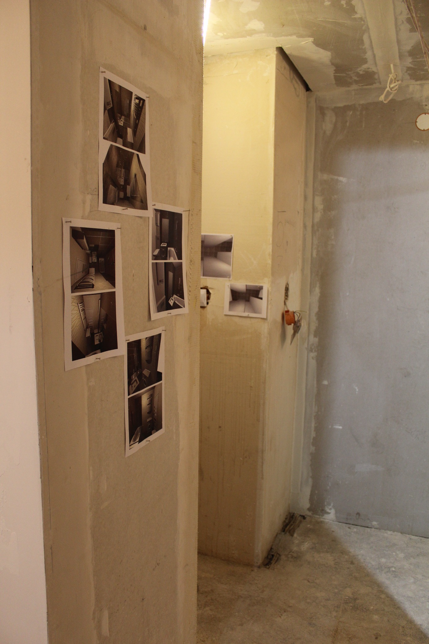 Surowy stan wnętrza w trakcie remontu: ściany w szarym tynku, na jednej z nich przyczepione zdjęcia łazienek, widoczne przewody elektryczne i klucze.