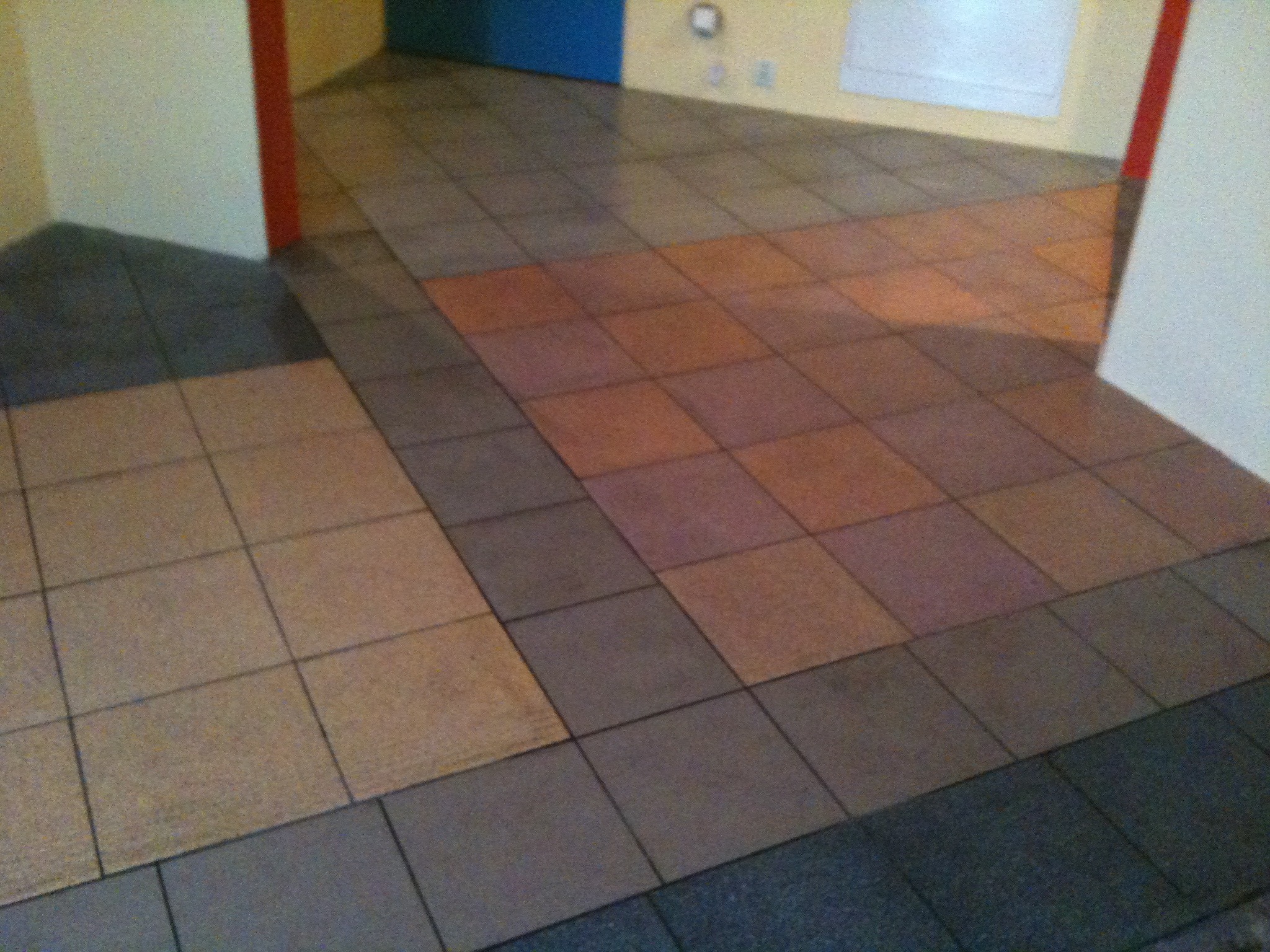 Różnokolorowa, kwadratowa podłoga z płytek w przejściu między pomieszczeniami, widoczne fragmenty ścian i drzwi.