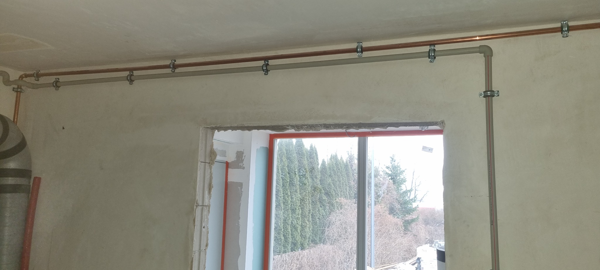 Montaż instalacji grzewczej w surowym stanie w Olsztynie, widoczne rury miedziane i plastikowe przymocowane do ściany nad oknem.