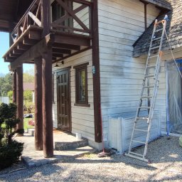 Adam Wieczorek - Dom z drewnianą elewacją w trakcie malowania na jasny kolor, widoczna drabina oparta o ścianę, fragmenty elewacji jeszcze niepomalowane, ukazujące pierwotny odcień drewna.