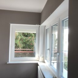 Adam Wieczorek - Ściana pomalowana na szaro, z białym oknem z widokiem na drzewa i balkon.