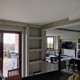 Wnętrze mieszkania po odświeżeniu ścian, widoczne wnęki w ścianach, drabina przy wyjściu na balkon i częściowo umeblowany salon w głębi.