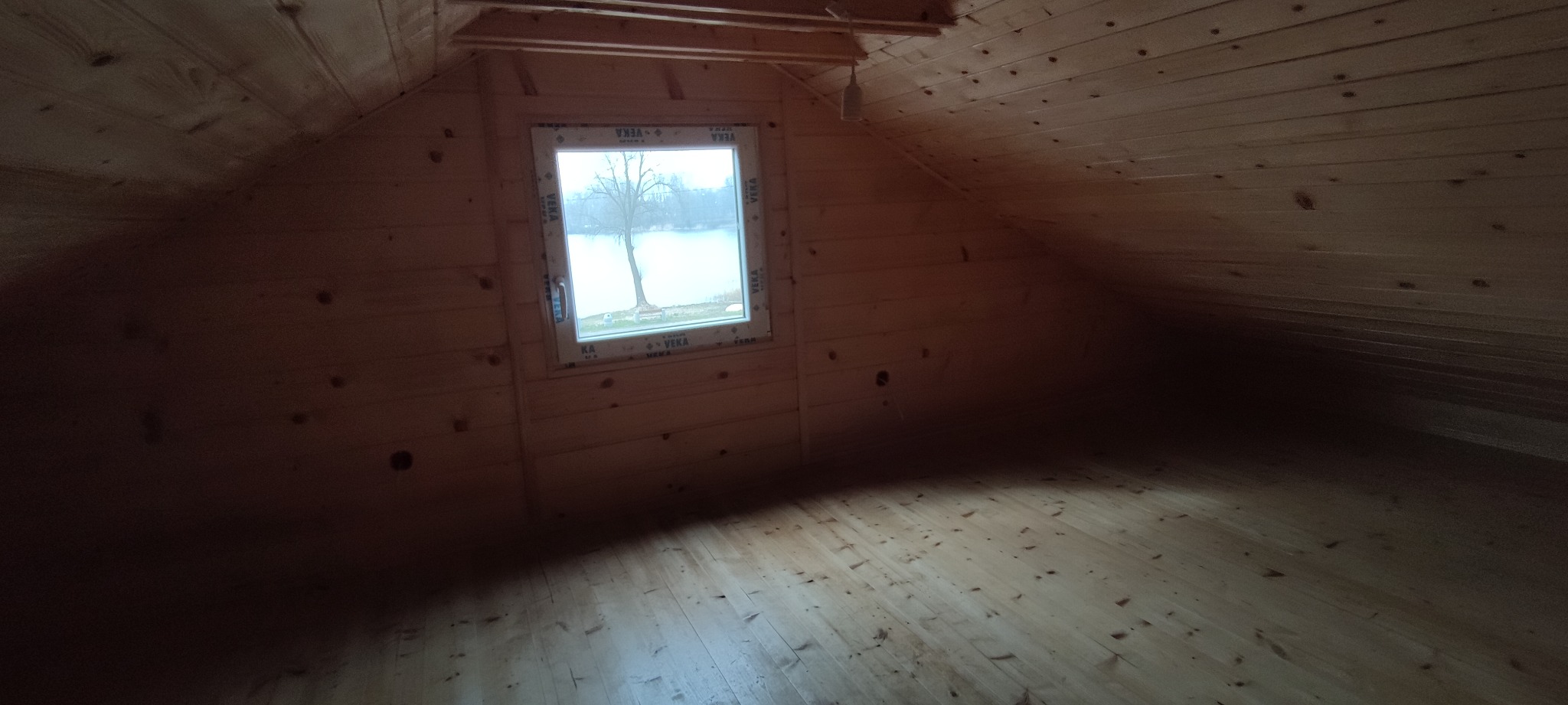 Poddasze wykończone boazerią, okno z widokiem na jezioro, surowy stan przed wykończeniem podłogi.