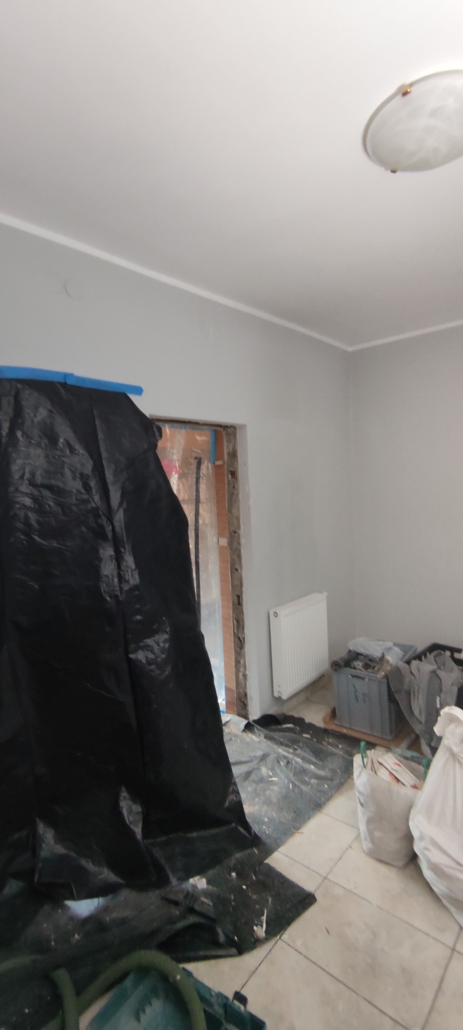 Pokój w trakcie remontu, zabezpieczony folią malarską, widoczne przygotowania do prac wykończeniowych, świeżo pomalowane szare ściany i grzejnik.