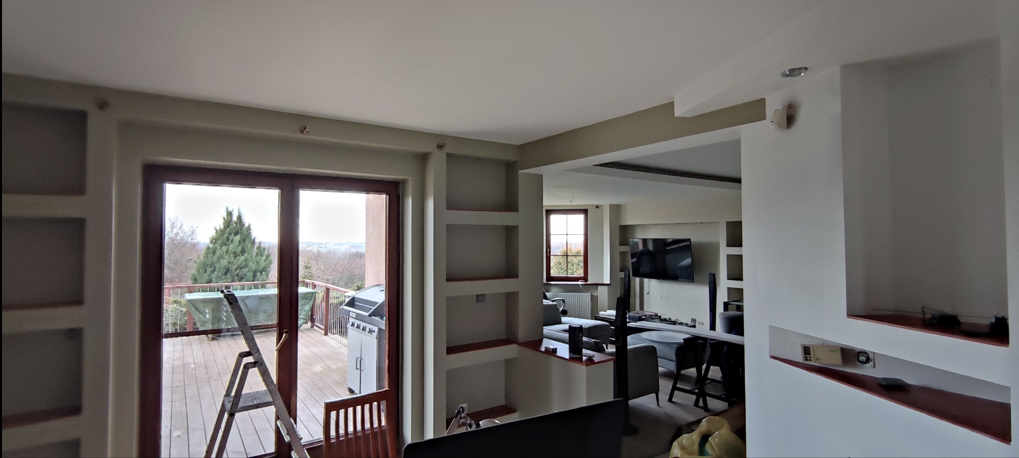 Wnętrze mieszkania po odświeżeniu ścian, widoczne wnęki w ścianach, drabina przy wyjściu na balkon i częściowo umeblowany salon w głębi.