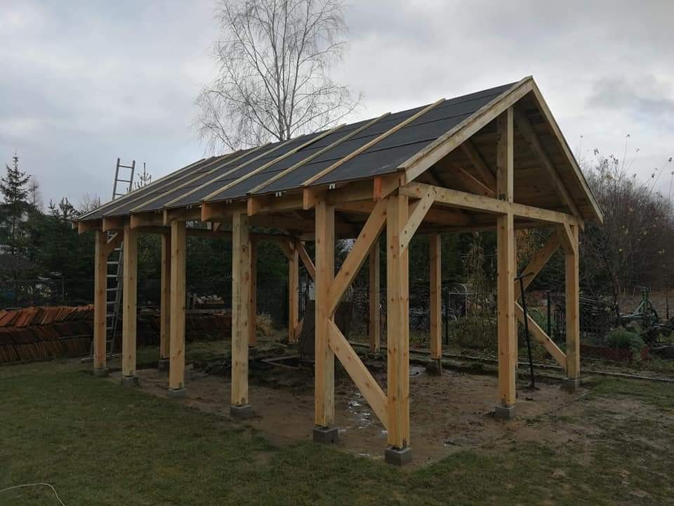 Drewniana konstrukcja z dachem z papy bitumicznej w trakcie budowy; widoczna drabina oparta o bok konstrukcji.