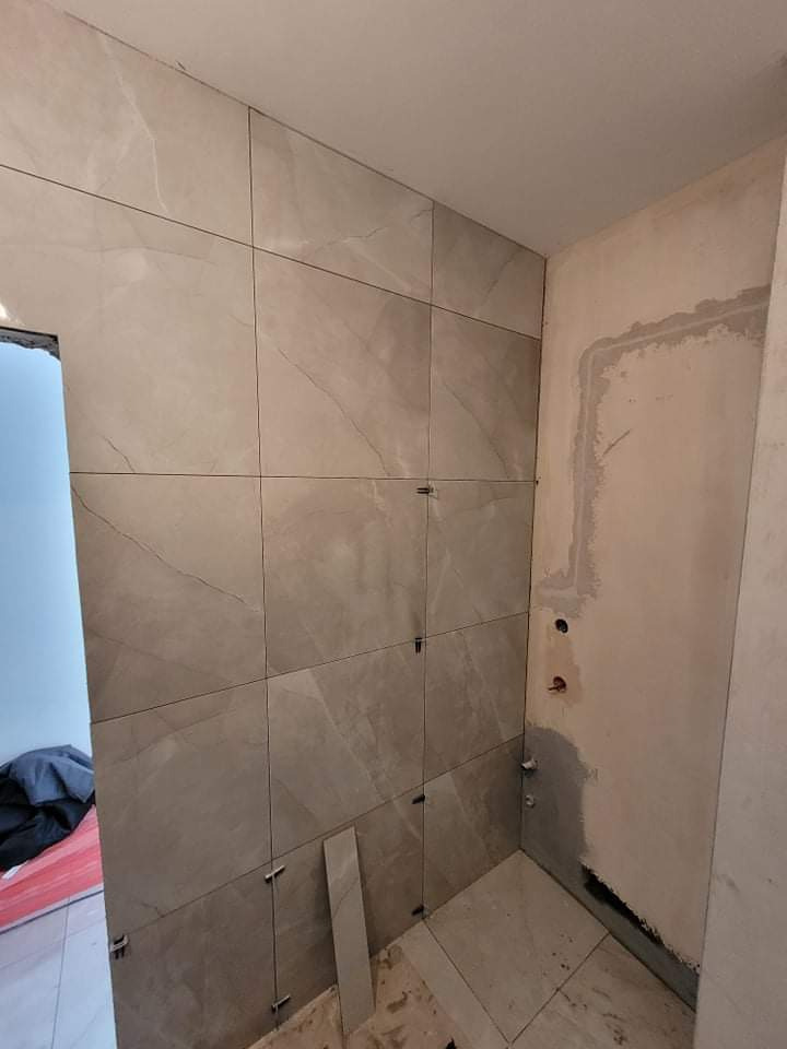 Ściana łazienki w trakcie układania płytek imitujących marmur, widoczne krzyżyki dystansowe, fragment ściany przygotowanej pod dalsze prace, instalacja hydrauliczna.