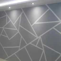 Ściana w pokoju pomalowana na szaro z białymi geometrycznymi wzorami, oświetlona przez punktowe lampy sufitowe.