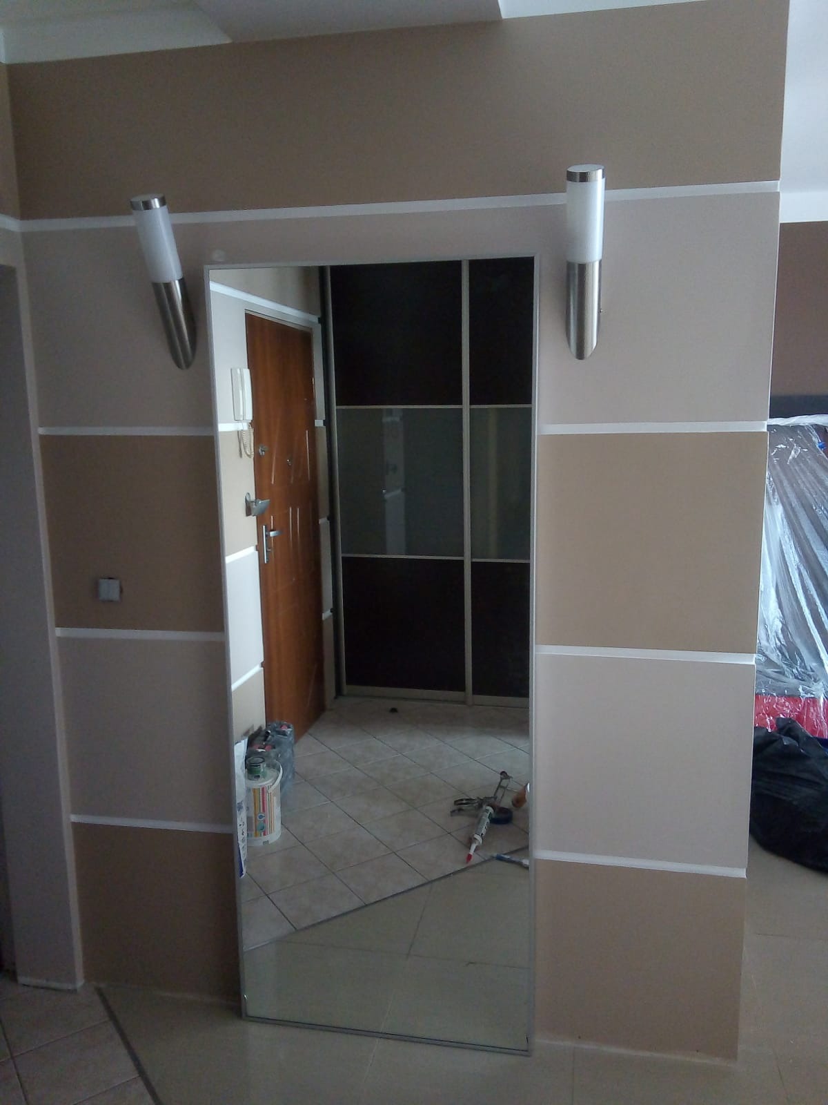 Korytarz po malowaniu z widocznym lustrem, lampami ściennymi i częściowo zasłoniętą szafą przesuwną w tle.