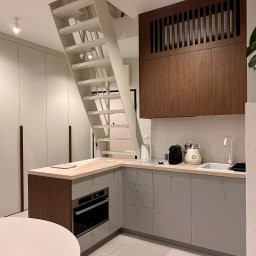 Binexus Michał Wojtaszuk - Nowoczesna kuchnia z białymi schodami metalowymi prowadzącymi na górę, drewniane akcenty i szare szafki. Minimalistyczny design z dbałością o detale.