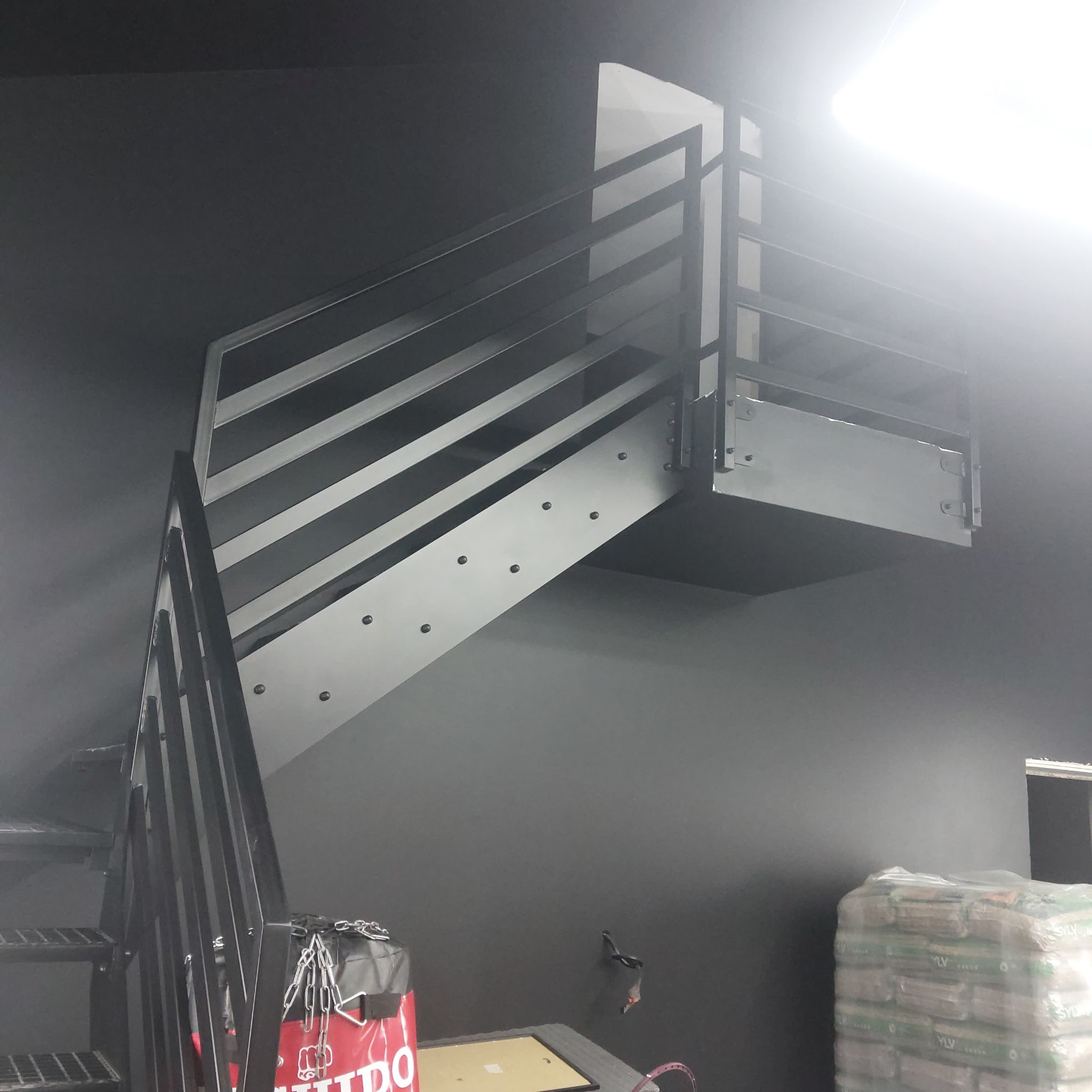 Nowoczesne schody metalowe z balustradą w Kurowie. Minimalistyczny design, czarne elementy konstrukcyjne, widoczne mocowania. Ujęcie z dołu, podkreślające solidność wykonania.