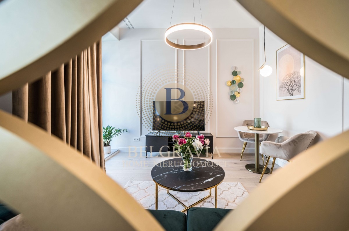 Elegancko urządzone wnętrze salonu z marmurowym stolikiem kawowym, kwiatami w wazonie, telewizorem na tle dekoracyjnej ściany i okrągłą lampą sufitową, widziane przez ażurową przegrodę.