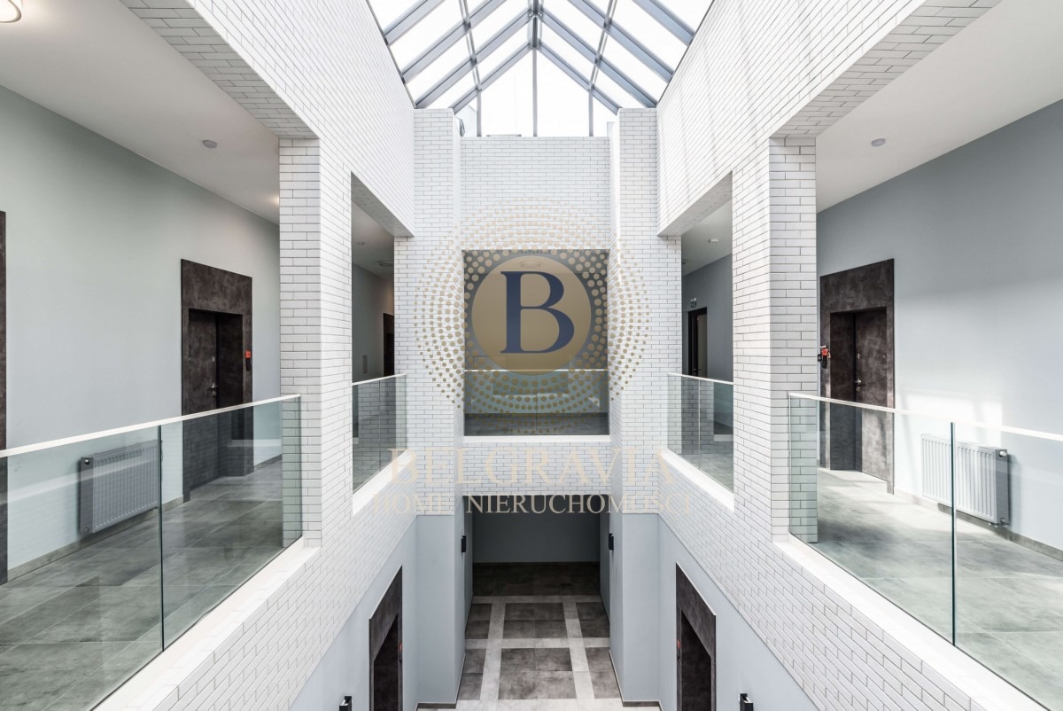 Wnętrze nowoczesnego budynku z przeszklonym dachem, białą cegłą, szklanymi balustradami i logo firmy na ścianie.
