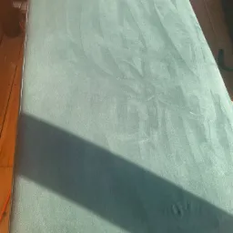 Zielony materac po praniu, widoczne ślady czyszczenia i cień na powierzchni, na drewnianym tarasie.