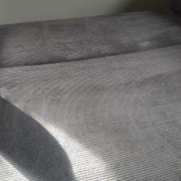 Szara kanapa z wyraźną fakturą materiału, z widocznym cieniem padającym na siedzisko. Widoczny fragment oparcia kanapy.