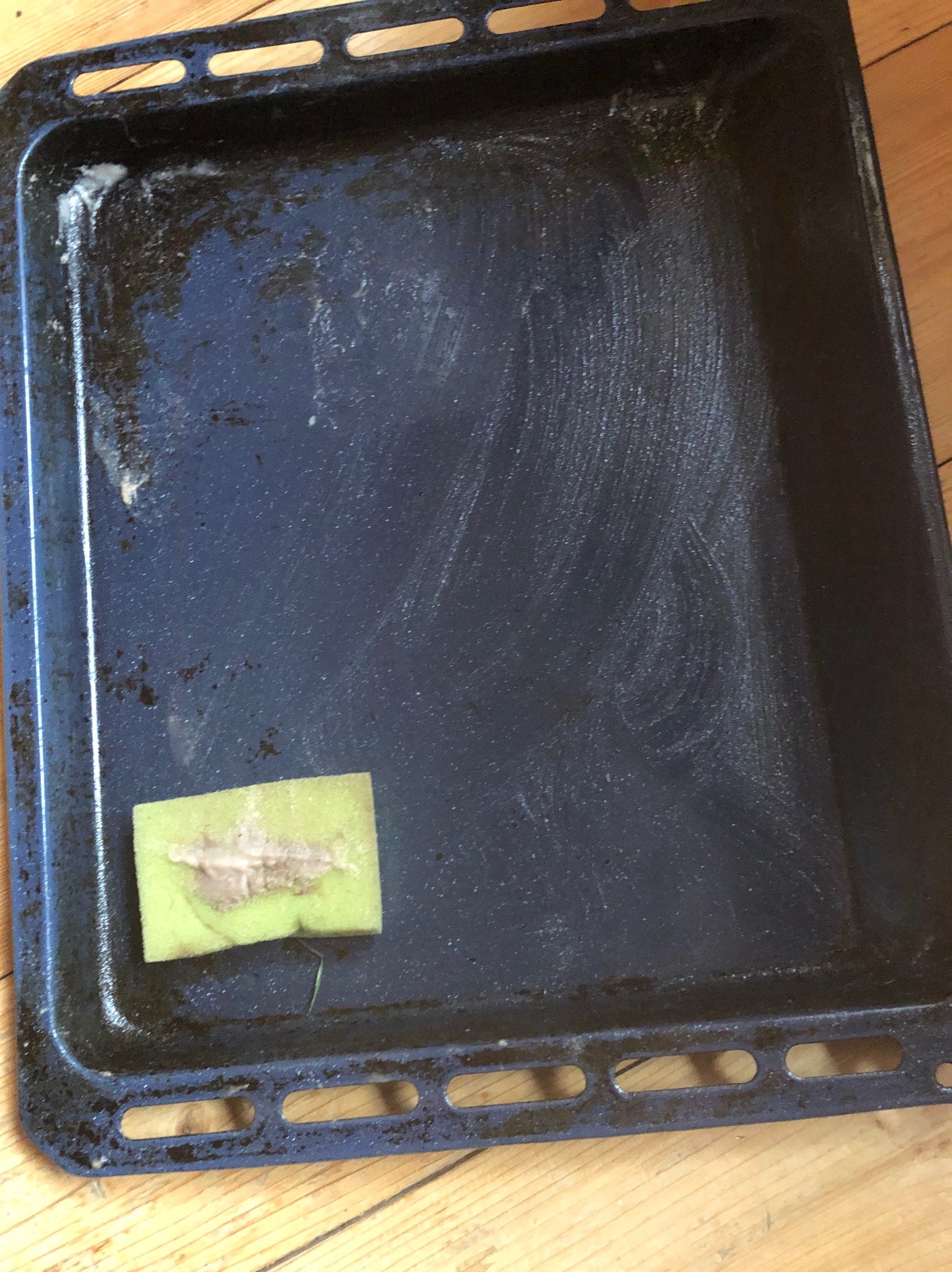 Brudna blacha do pieczenia z resztkami jedzenia i gąbką czyszczącą na drewnianej powierzchni.