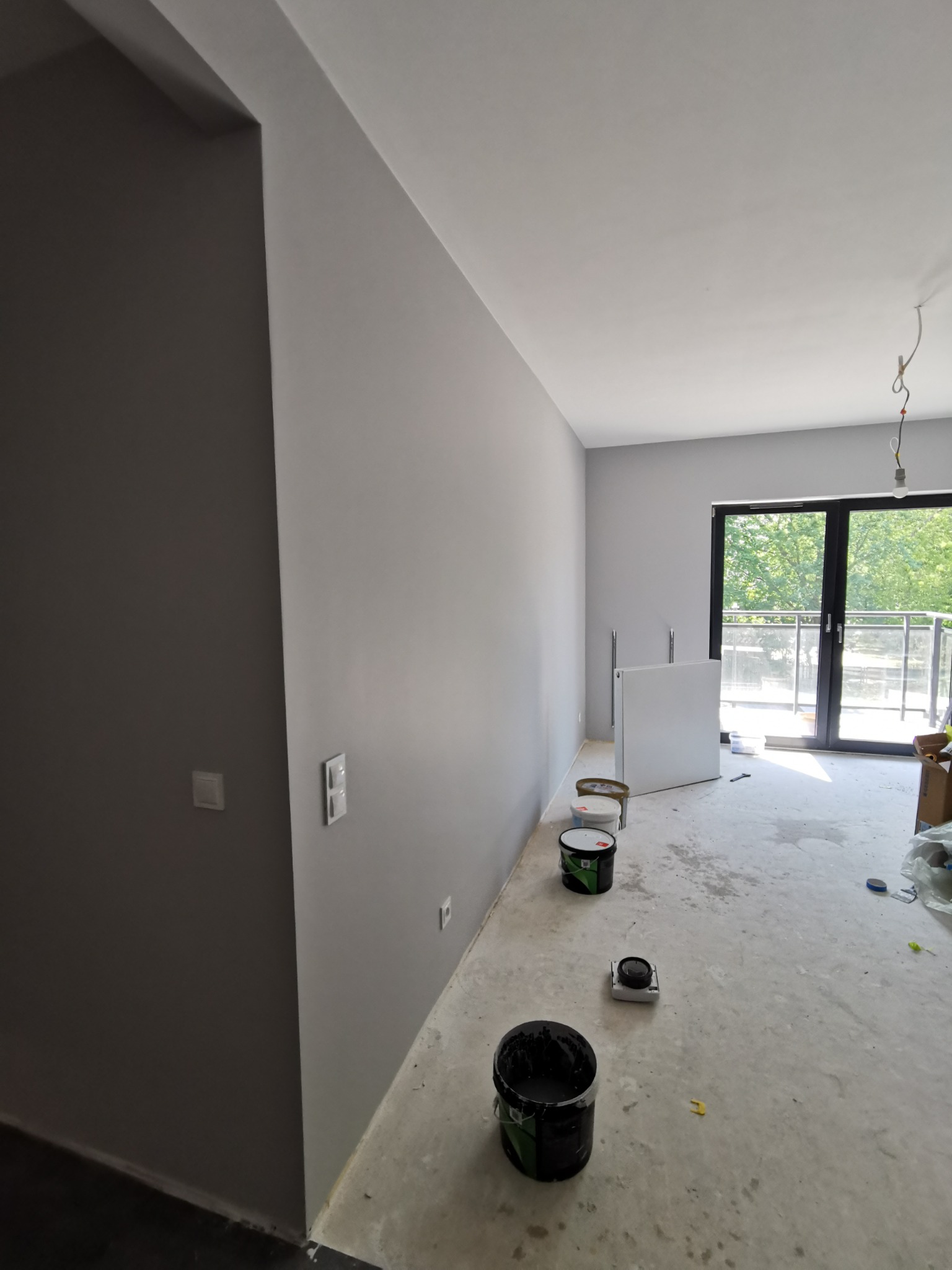 Świeżo pomalowane na szaro mieszkanie z widocznymi puszkami farby i balkonem w tle.