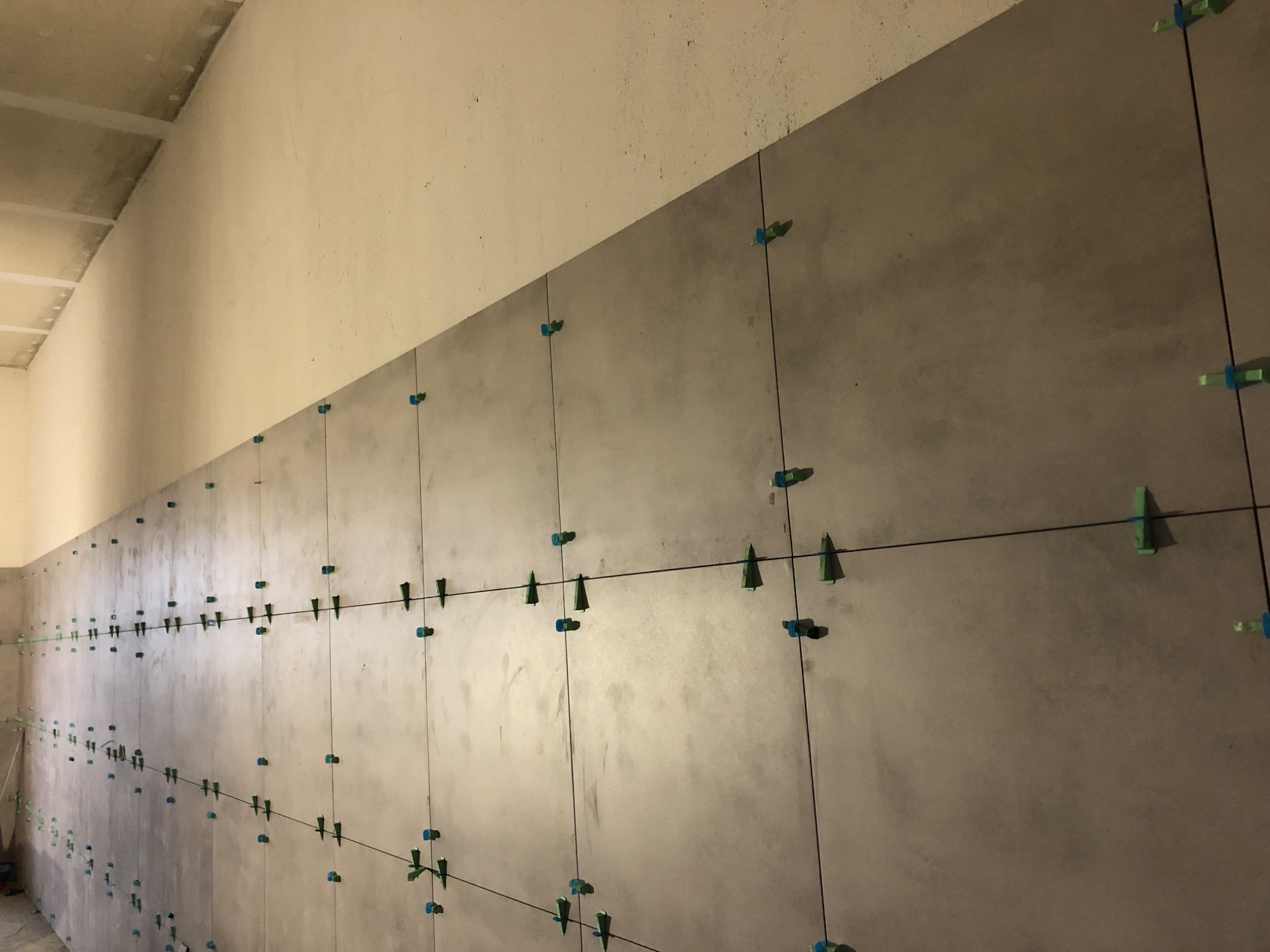 Montaż szarych płytek wielkoformatowych na ścianie z użyciem krzyżyków dystansowych i sznurka do poziomowania.