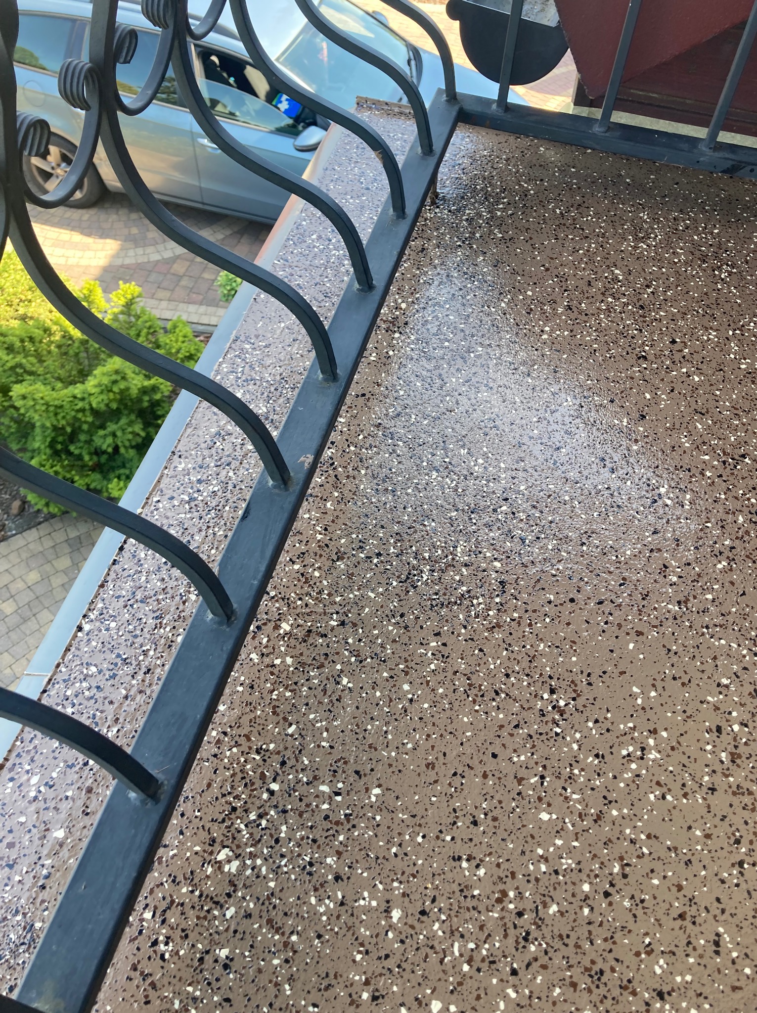 Balkon z żywiczną posadzką w odcieniach brązu i czerni, wykończony metalową balustradą. Widok z góry na gładką, błyszczącą powierzchnię i elementy otoczenia.
