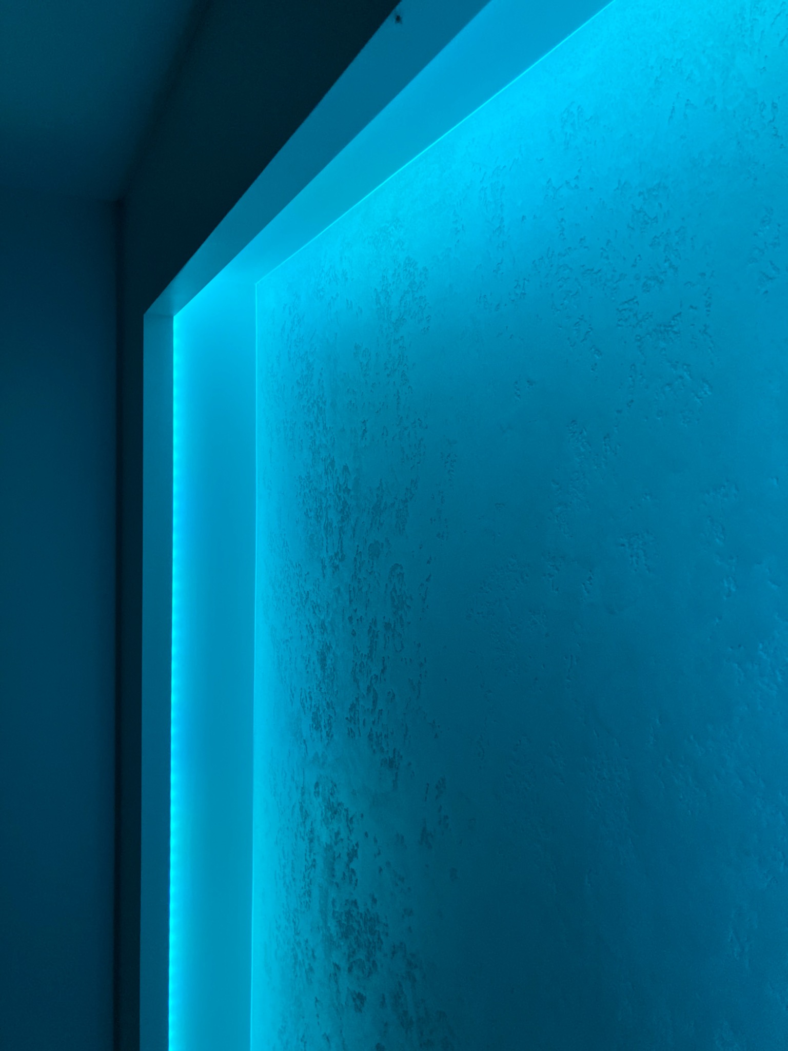 Ściana z dekoracyjną strukturą oświetlona intensywnym, niebieskim światłem LED wzdłuż krawędzi wnęki.