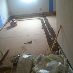 MarioBau Mariusz Górecki - Poddasze w trakcie prac: widoczne płyty izolacyjne Pavatex, poziomica, ślady po cięciu oraz narzędzie na podłodze, niebieski pas na ścianie, surowe drewniane krokwie.