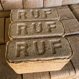 Etna Zbigniew Przepiórski - Stos ułożonych brykietów drzewnych RUF z widocznym tłoczeniem napisu na każdym z nich, ukazujący strukturę włókien drzewnych.