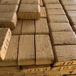 Etna Zbigniew Przepiórski - Ułożone w stosy brykiety drzewne z widocznym napisem 'RUF' na niektórych kostkach, ukazujące teksturę drewna i charakterystyczne pęknięcia.