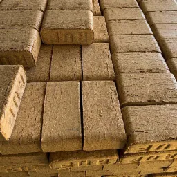 Ułożone w stosy brykiety drzewne z widocznym napisem 'RUF' na niektórych kostkach, ukazujące teksturę drewna i charakterystyczne pęknięcia.