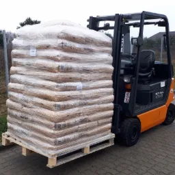 Wózek widłowy STILL R70-16 transportuje paletę z workami pelletu, owiniętą folią stretch na zewnątrz, widoczne etykiety na workach.