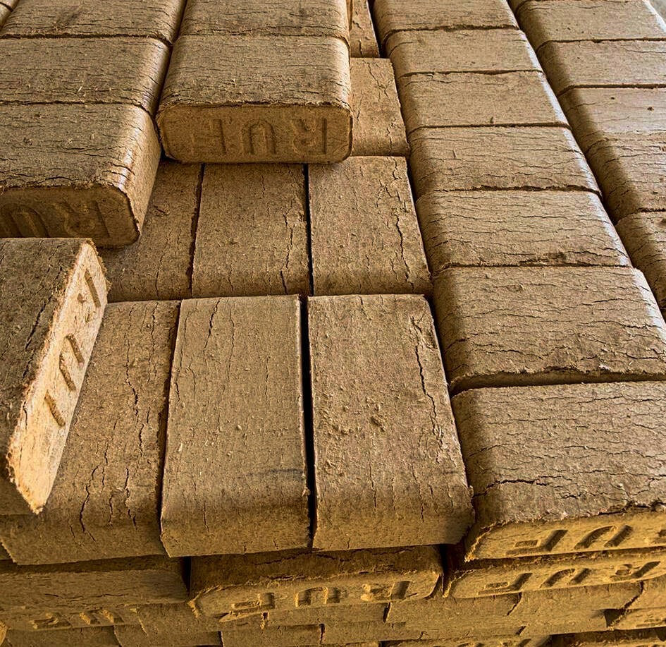 Ułożone w stosy brykiety drzewne z widocznym napisem 'RUF' na niektórych kostkach, ukazujące teksturę drewna i charakterystyczne pęknięcia.