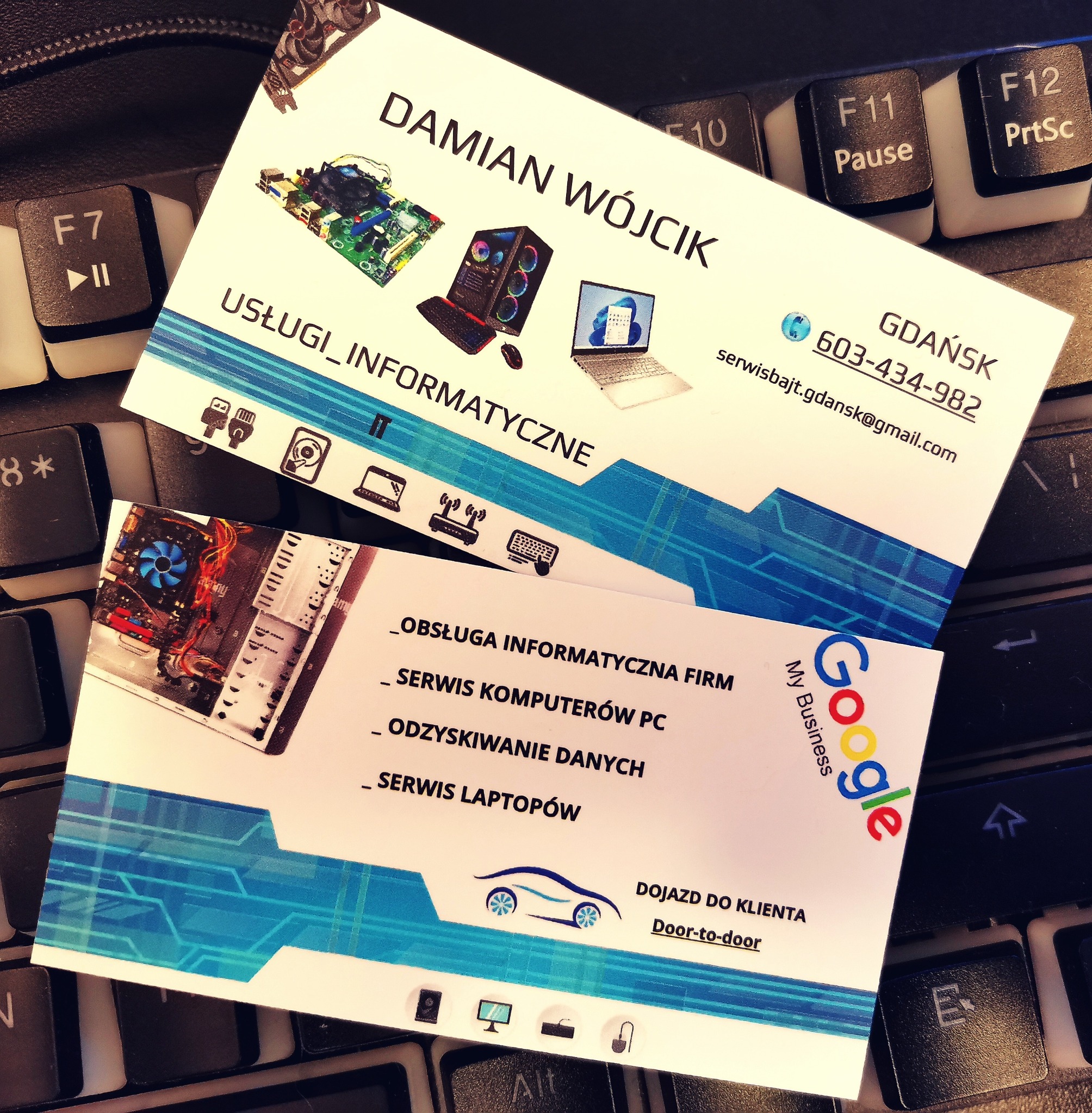 Dwie wizytówki firmy informatycznej Damian Wójcik leżące na klawiaturze komputera, oferującej obsługę informatyczną firm, serwis komputerów PC, odzyskiwanie danych i serwis laptopów, z dojazdem...