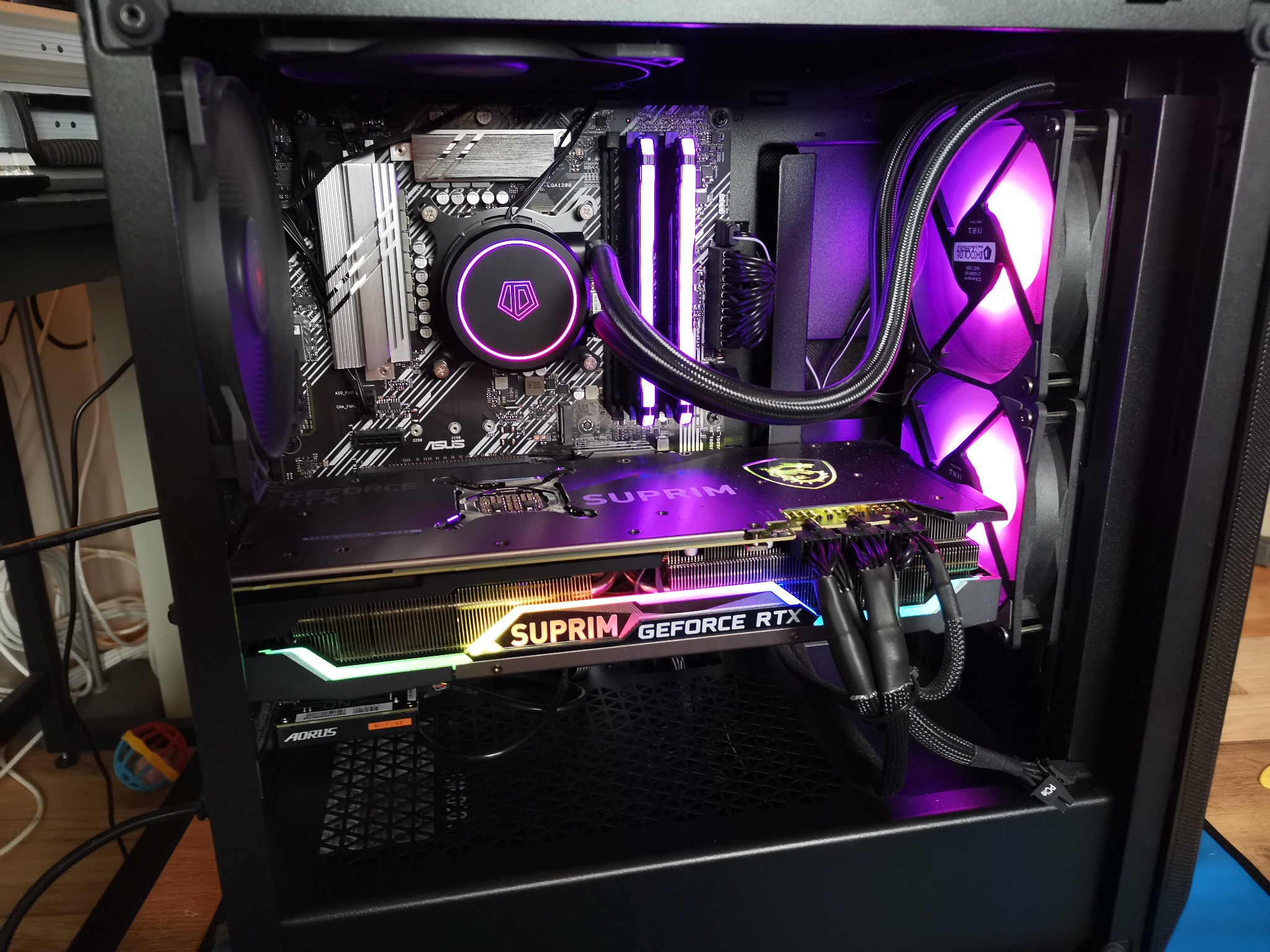 Wnętrze czarnej obudowy komputera stacjonarnego z podświetleniem RGB, widoczna karta graficzna MSI Suprim GeForce RTX, chłodzenie wodne procesora ID-Cooling z fioletowym podświetleniem, pamięć RAM...