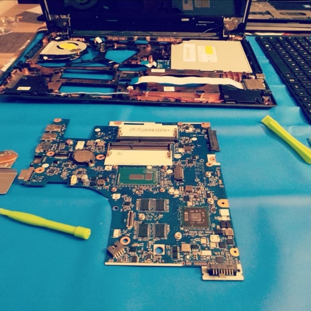 Płyta główna laptopa z widocznym procesorem, obok rozłożony laptop i zielone narzędzia na niebieskim podłożu.