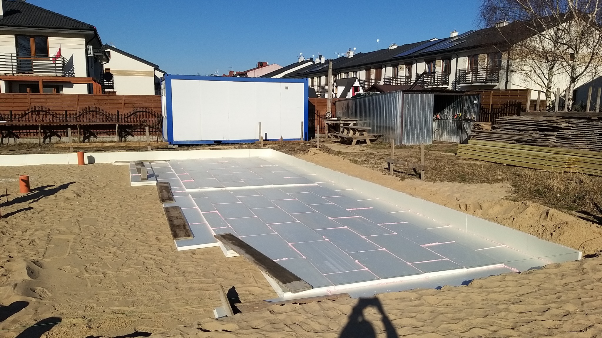 Przygotowany teren pod budowę z izolacją fundamentów w postaci płyt styropianowych, widoczny kontener budowlany, w tle zabudowa jednorodzinna.