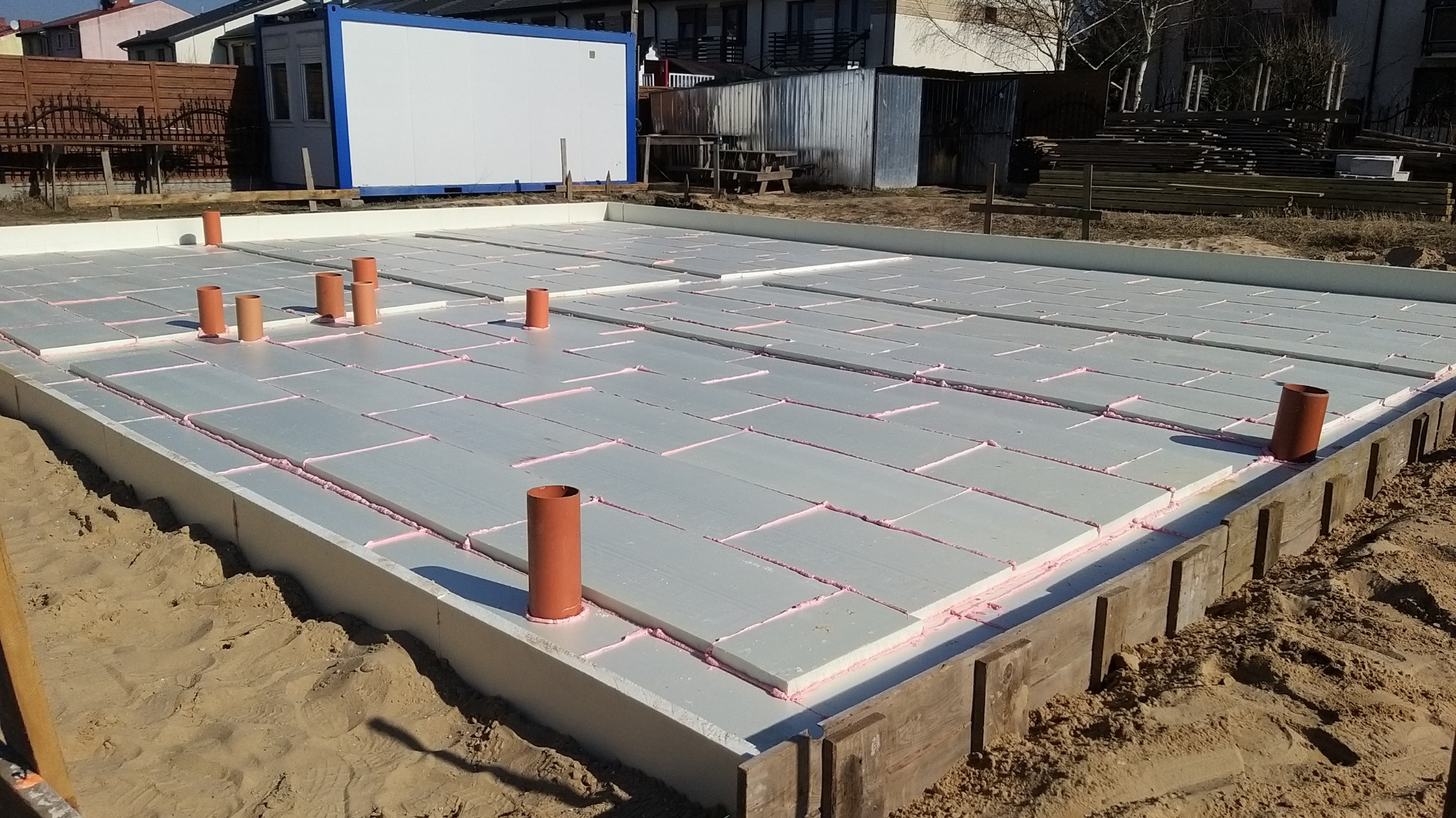 Przygotowanie fundamentów pod budynek: izolacja termiczna ze styropianu ekstrudowanego, uszczelniona różową pianką, z pionowymi rurami kanalizacyjnymi.