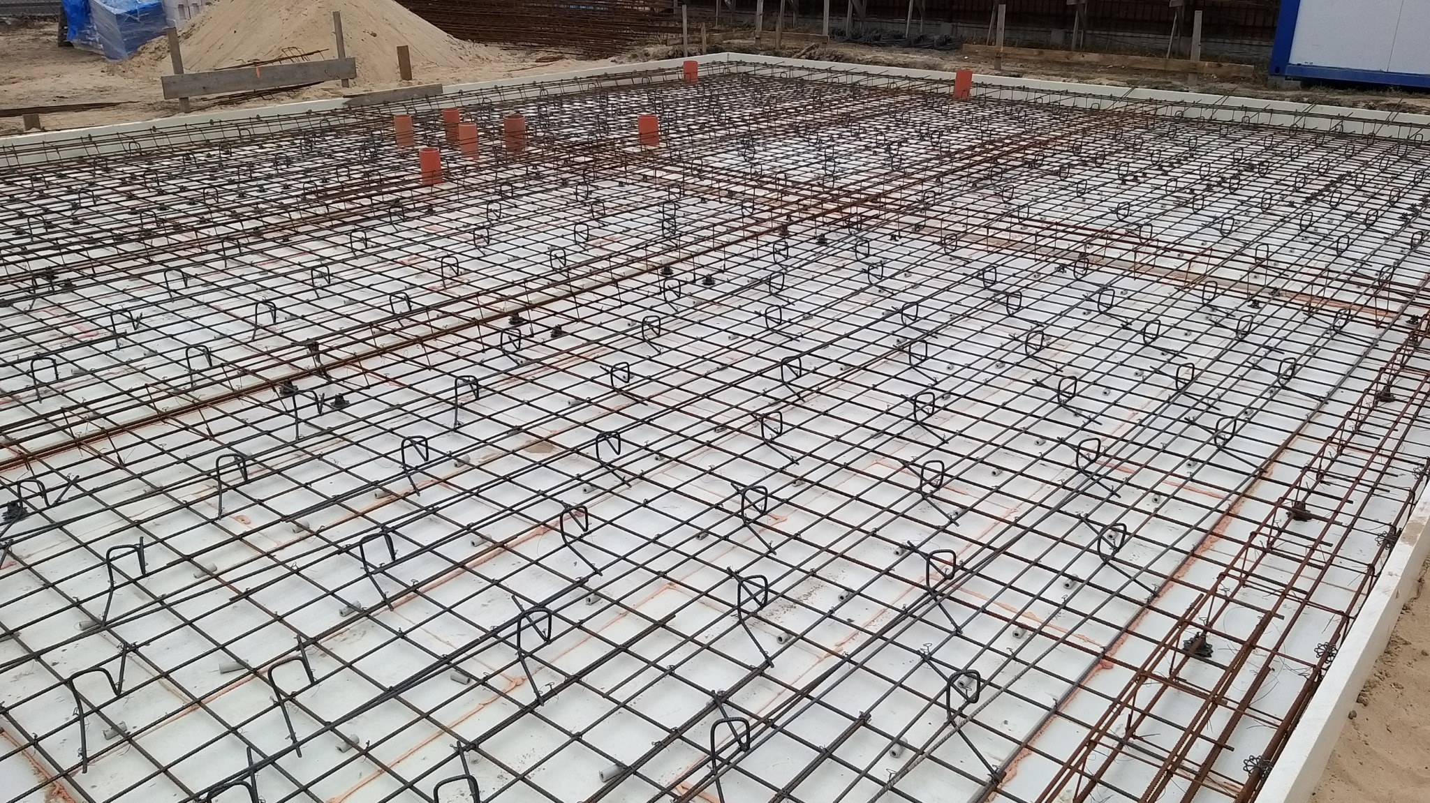 Siatka zbrojeniowa fundamentu z widocznymi elementami dystansowymi i rurami instalacyjnymi, przygotowana do zalania betonem.