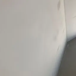 Świeżo wyszpachlowana ściana w rogu pomieszczenia, widoczne delikatne nier&oacute;wności i ślady po szpachli, przygotowana do dalszych prac wykończeniowych.