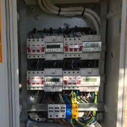 Rozdzielnica elektryczna z licznikami energii dla mieszkań w Bielsku-Białej, widoczne kable, bezpieczniki i oznaczenia pięter.