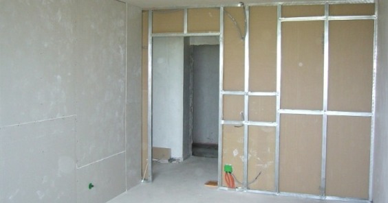 Stelaż z profili metalowych i płyt kartonowo-gipsowych tworzący ścianę działową z otworem drzwiowym, widoczne przewody elektryczne w puszce.