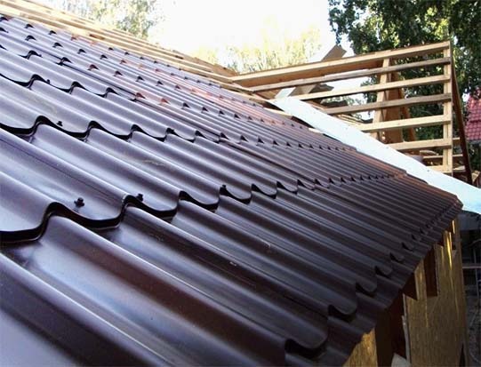 Montaż brązowej blachy trapezowej na dachu z widoczną drewnianą konstrukcją szkieletową.