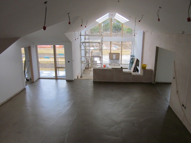 Wnętrze w trakcie remontu z wylaną posadzką, widoczne okna, rusztowanie i przygotowane ściany do szpachlowania.