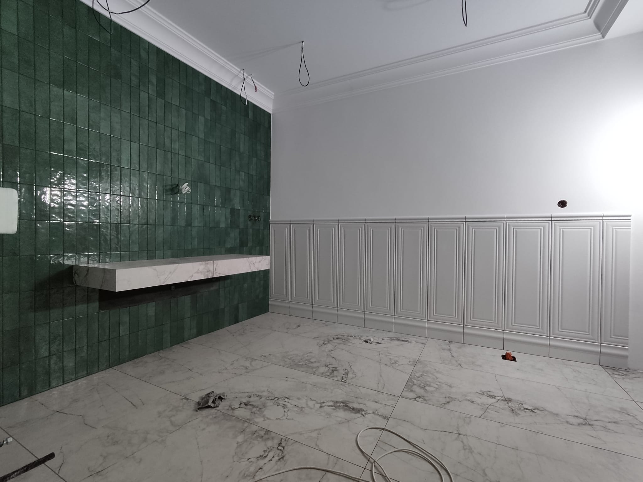 Wykończona łazienka z zielonymi, pionowo ułożonymi płytkami na ścianie, marmurową półką i dekoracyjną białą boazerią. Podłoga wyłożona marmurowymi płytami.