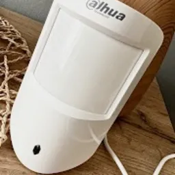 Biały czujnik ruchu Dahua z widocznym kablem na drewnianym tle.