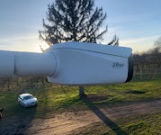 Biała kamera monitoringu marki Dahua zamontowana na zewnątrz, z widocznym samochodem i drzewami w tle, uchwycona w promieniach zachodzącego słońca.