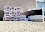 Stos pudełek z kamerami monitoringu i rejestratorem, ułożonych na betonowym podłożu w słoneczny dzień.