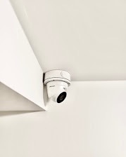 Kopułkowa kamera monitoringu CCTV zamontowana na białym suficie w rogu pomieszczenia, widok z dołu.