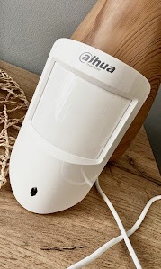 Biały czujnik ruchu Dahua z widocznym kablem na drewnianym tle.