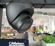 Kamera monitoringu kopułkowa, czarna, zamontowana pod sufitem w biurze z widocznym logotypem CAMeleon Monitoring w lewym dolnym rogu kadru.