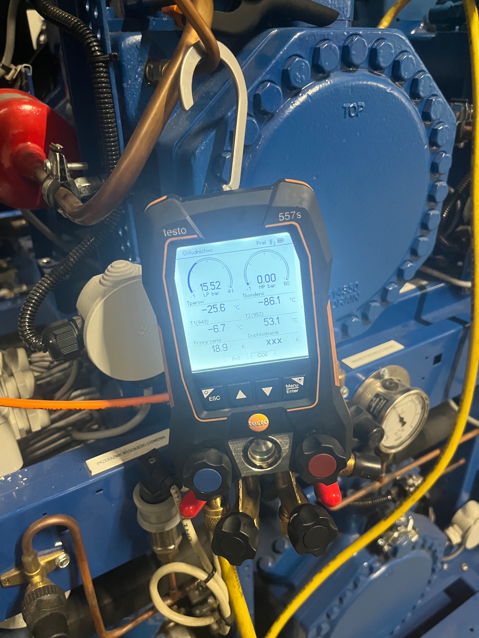 Miernik cyfrowy Testo 557s podłączony do niebieskiej sprężarki chłodniczej, wskazujący odczyty parametrów pracy układu chłodniczego.