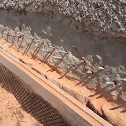 Przygotowanie wykopu pod fundamenty z widocznymi kotwami w ścianie i perforowaną płytą ochronną, grunt piaszczysty.